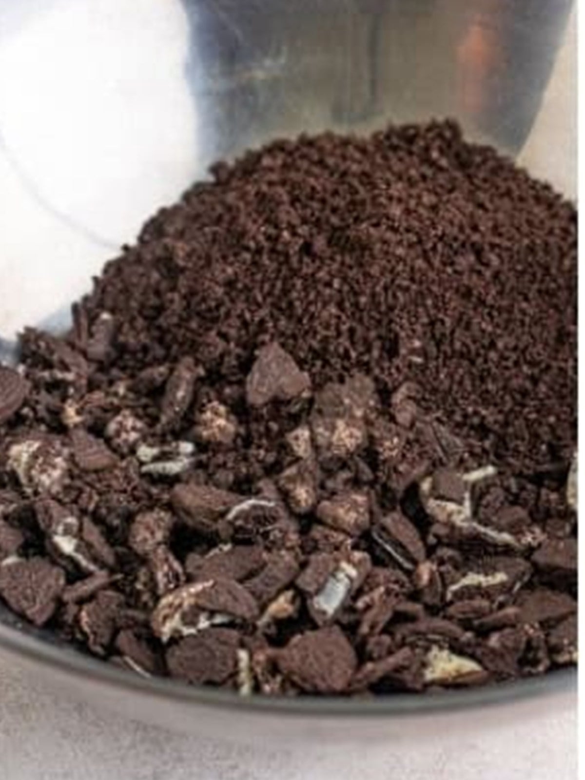 Crushed Oreos tossed with melted butter in a metal bowl for dirt cake.