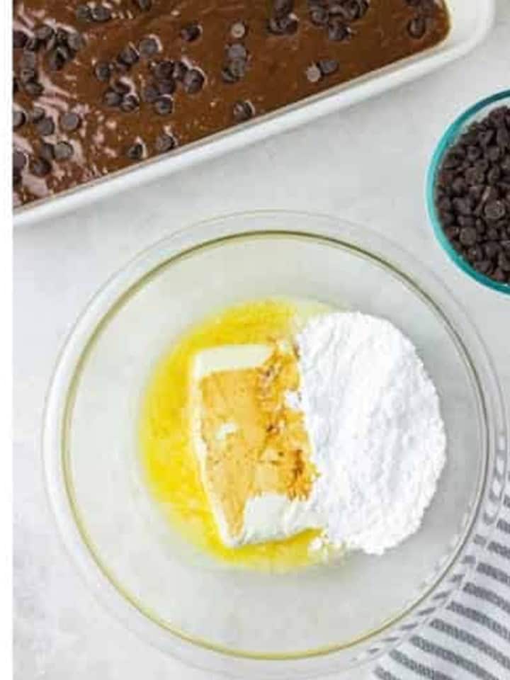 Melted butter, cream cheese, and powdered sugar in a glass bowl ready to be mixed.
