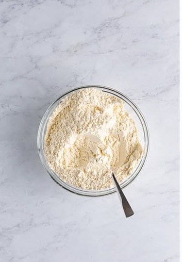 Flour, baking powder, baking soda, and salt whisked together in a glass bowl.