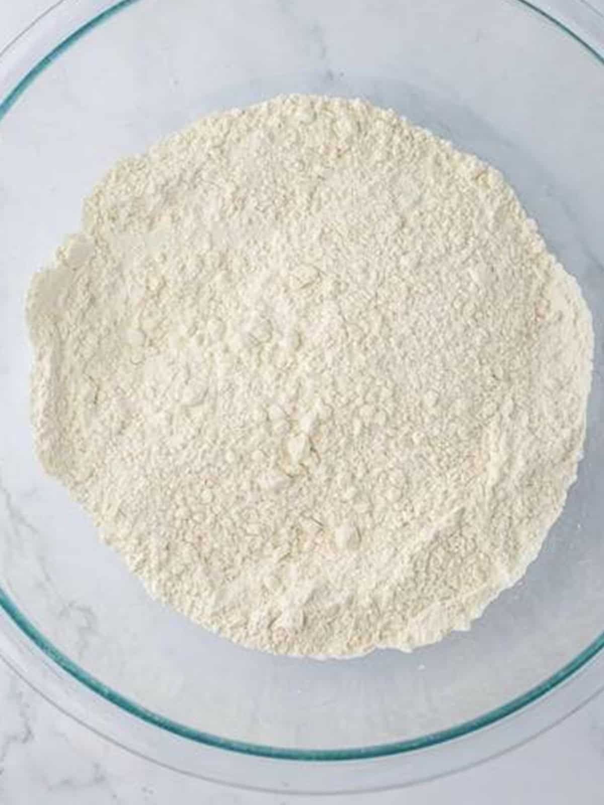 Flour, baking soda, baking powder, and salt stirred together in a glass mixing bowl.
