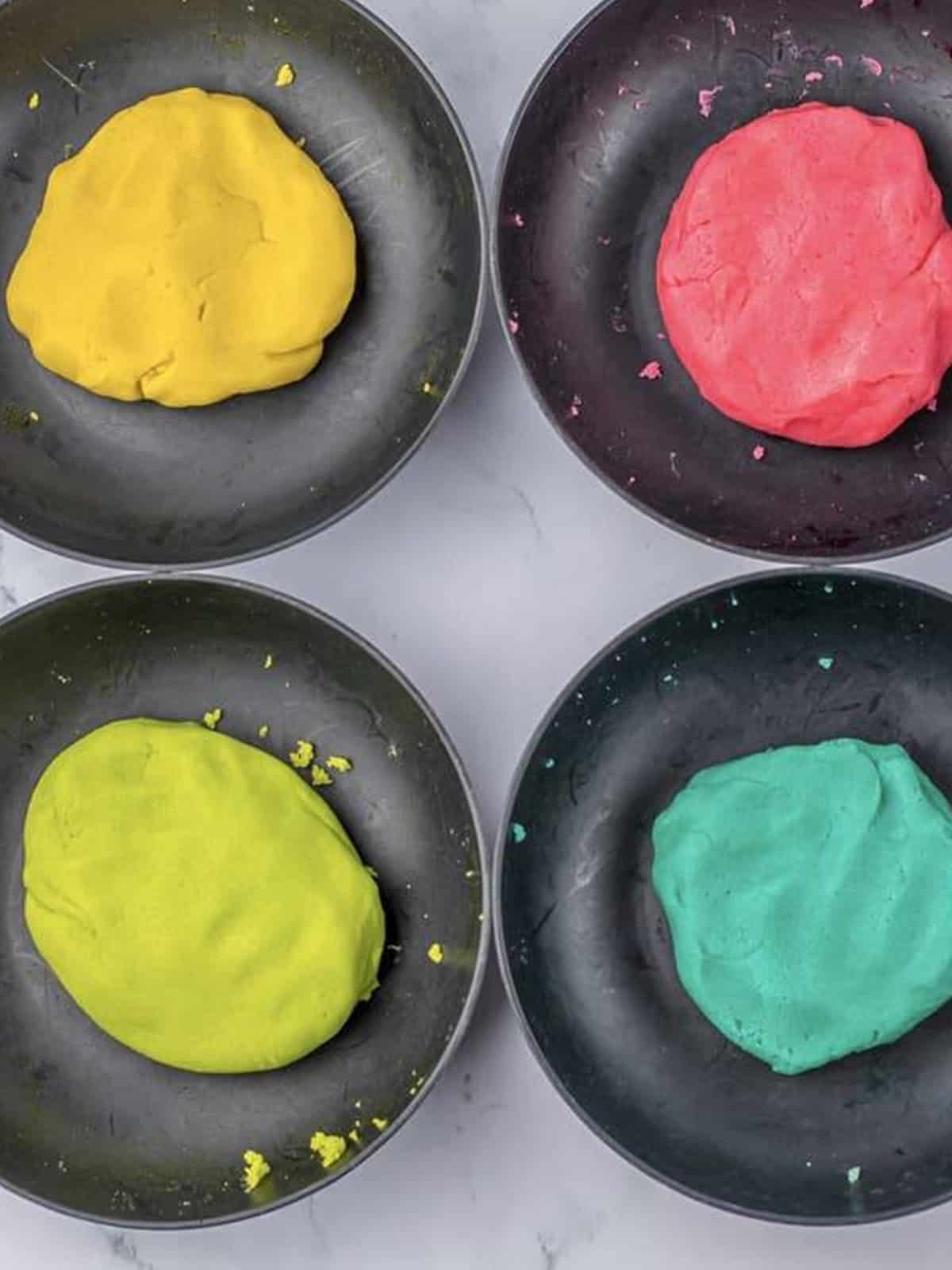 Sugar cookie dough divided into four bowls and tinted yellow, pink, green, and teal with gel food coloring.