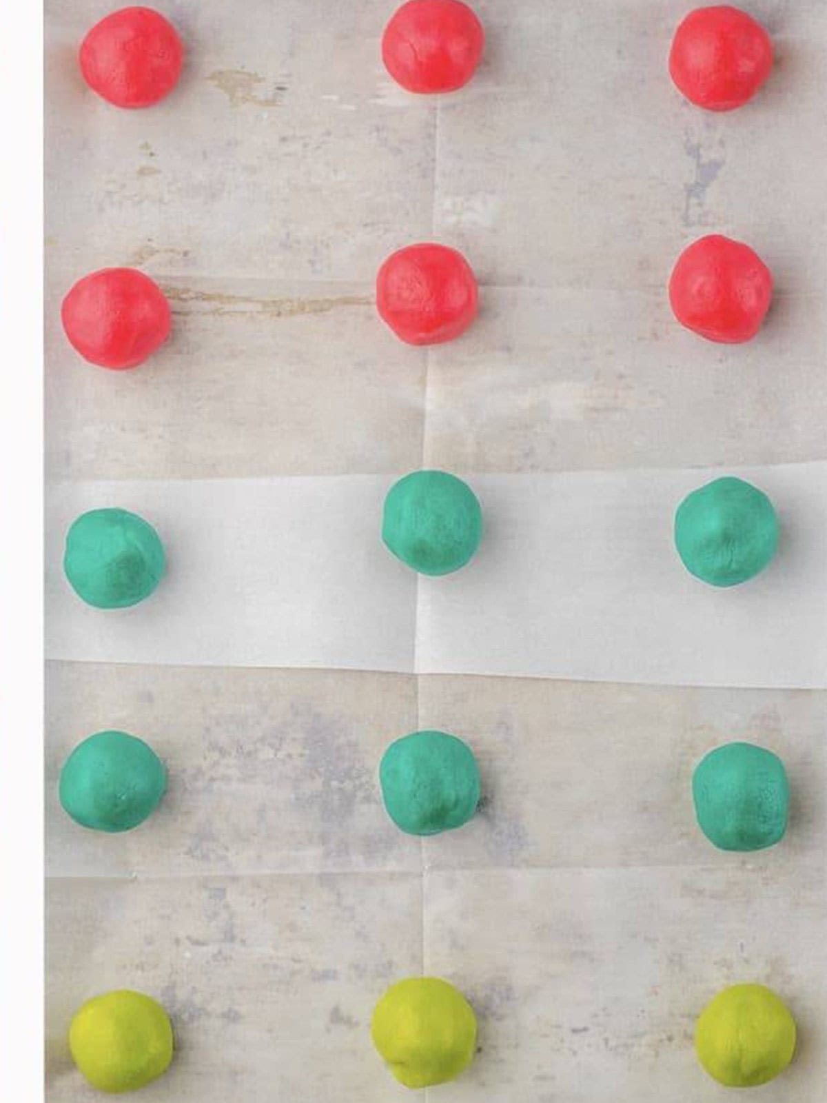 Pink, teal, and green Easter sugar cookie dough balls rolled and spaced on a parchment lined baking sheet.