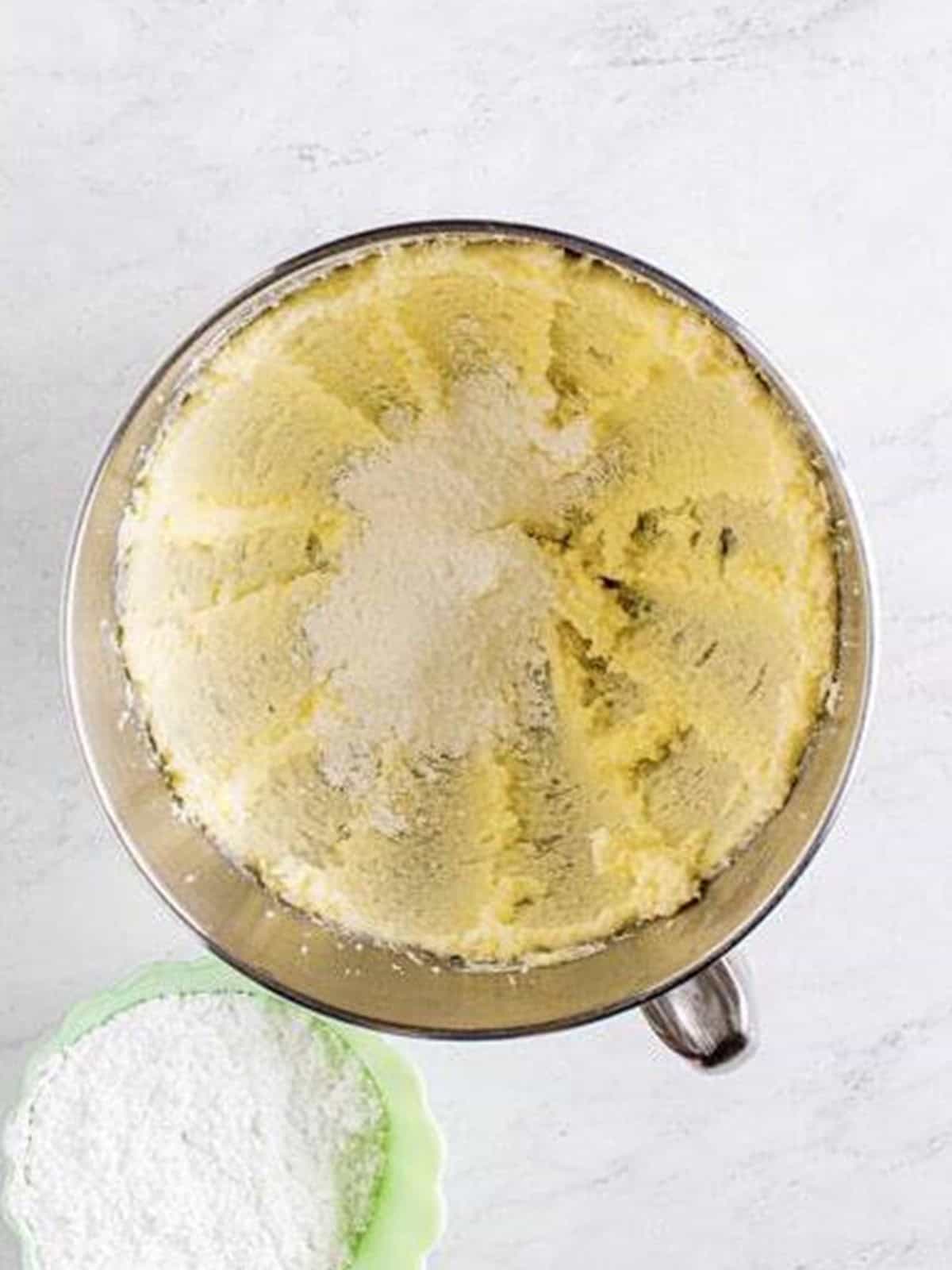 Powdered sugar being added to the creamed butter mixture for edible sugar cookie dough.