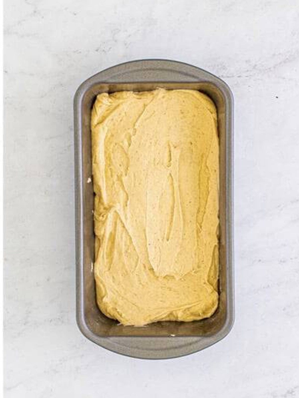 Eggnog bread batter spread into a prepared loaf pan ready to bake.