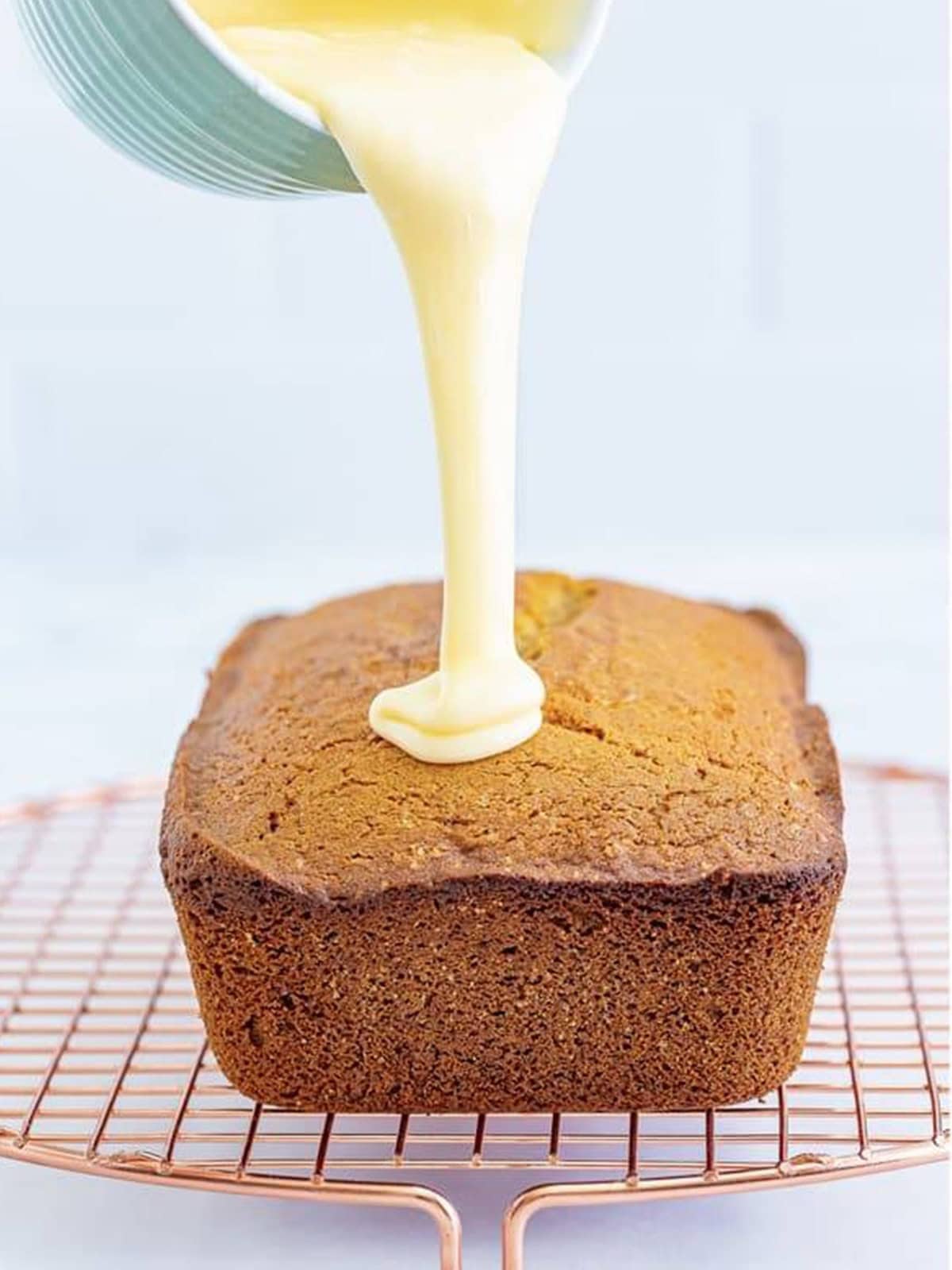 Eggnog glaze being poured over the cooled loaf of eggnog bread.
