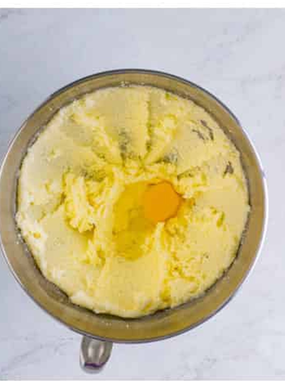 Adding eggs to the creamed butter and sugar in the mixer bowl.
