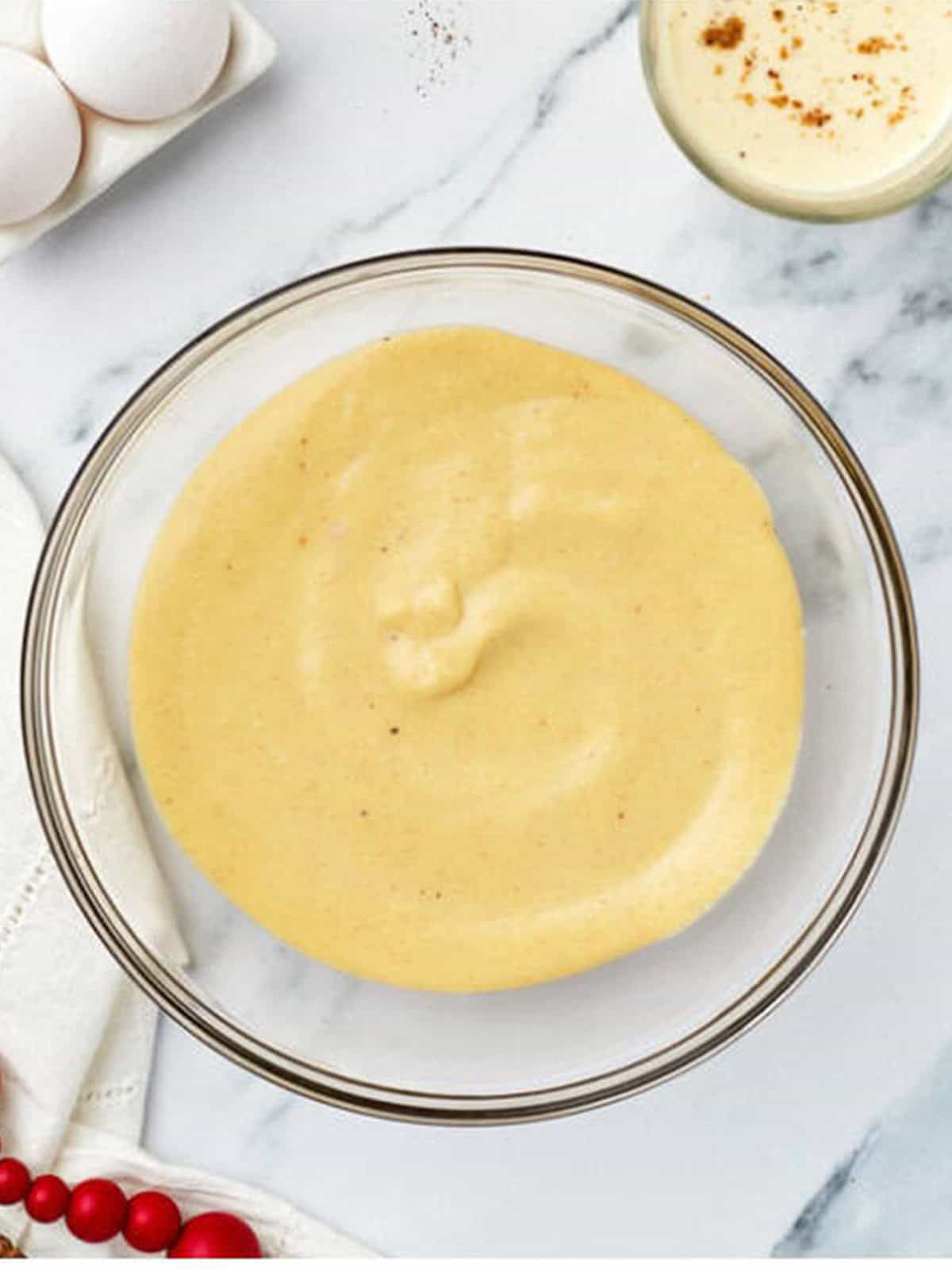 Thickened eggnog pudding in a glass bowl ready to chill until set.