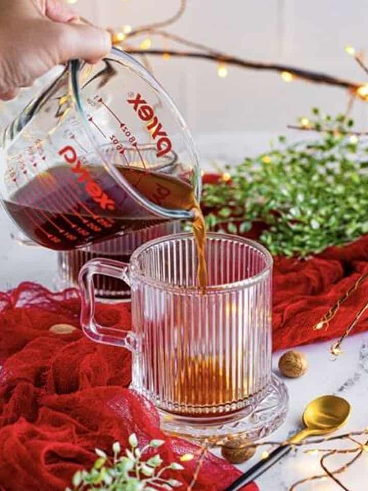 Pouring strong coffee into a glass mug for an Eggnog Latte.