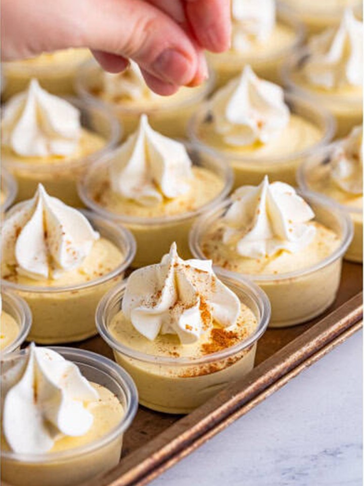 Whipped topping piped onto each eggnog pudding shot with a sprinkle of cinnamon.