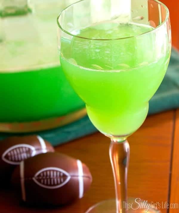 A glass of green football punch with lime sherbet foam next to chocolate footballs.