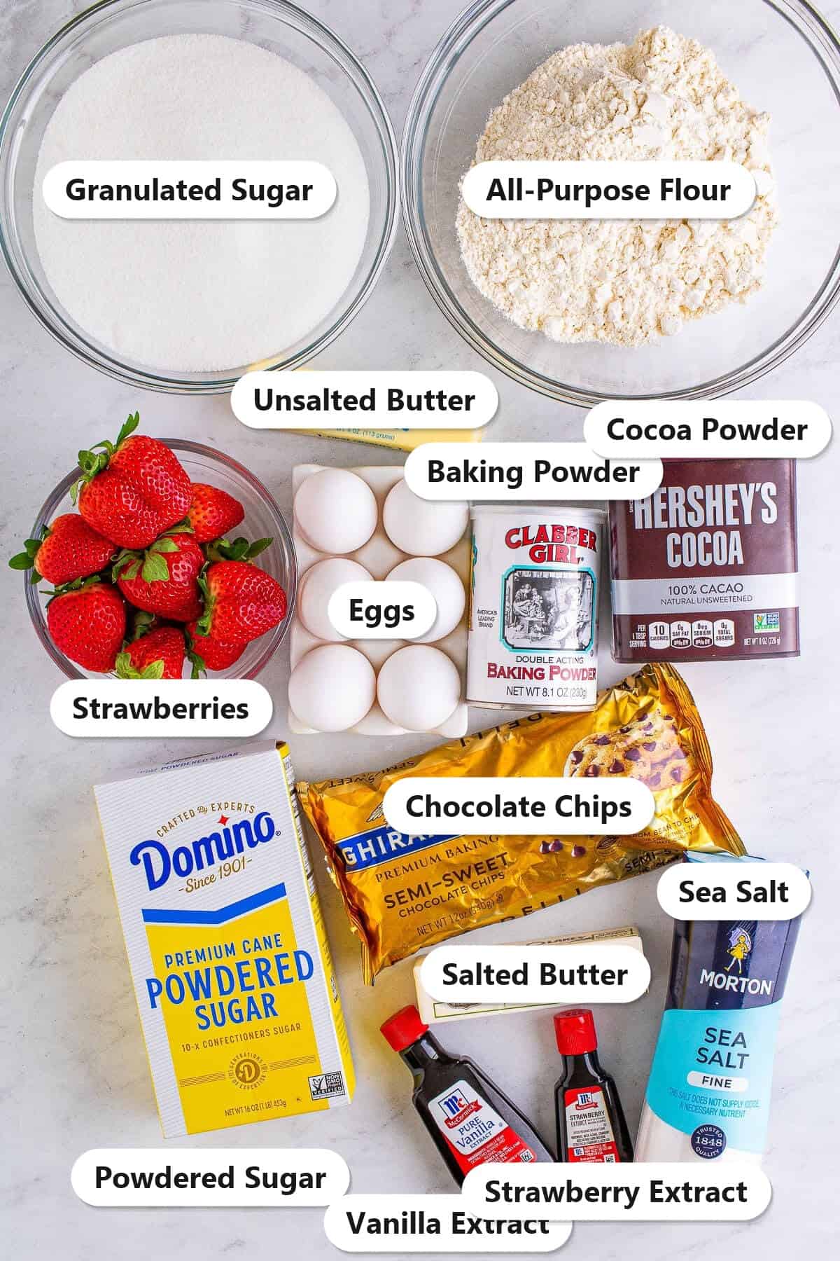 Labeled ingredients for frosted brownies including granulated sugar, all-purpose flour, cocoa powder, chocolate chips, butter, eggs, strawberries, powdered sugar, and extracts.
