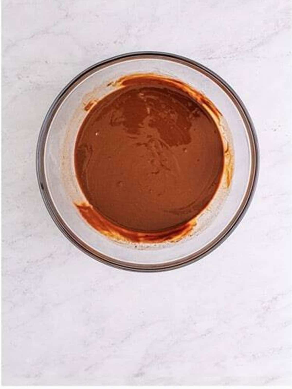 Melted chocolate and butter stirred smooth in a glass bowl for frosted brownies.