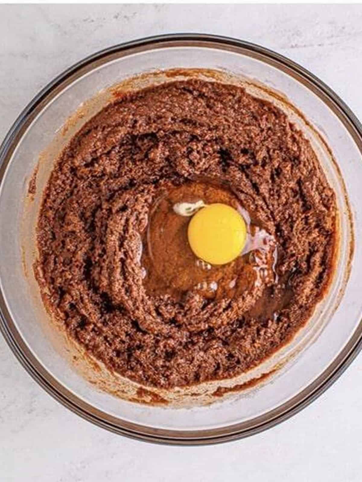 Egg being mixed into the sugar and chocolate mixture for frosted brownie batter.