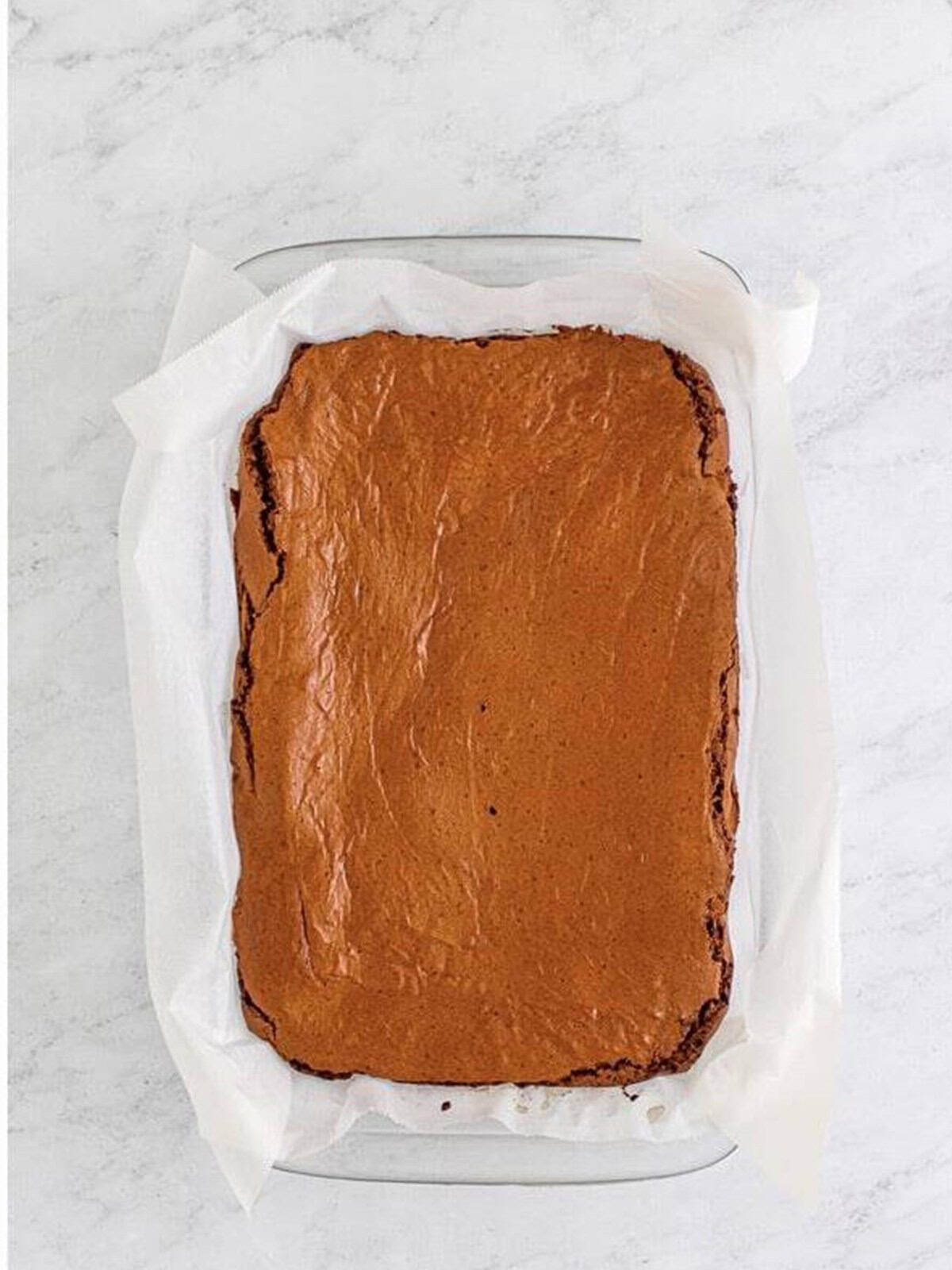 Baked chocolate brownie slab cooling in a parchment lined baking dish.