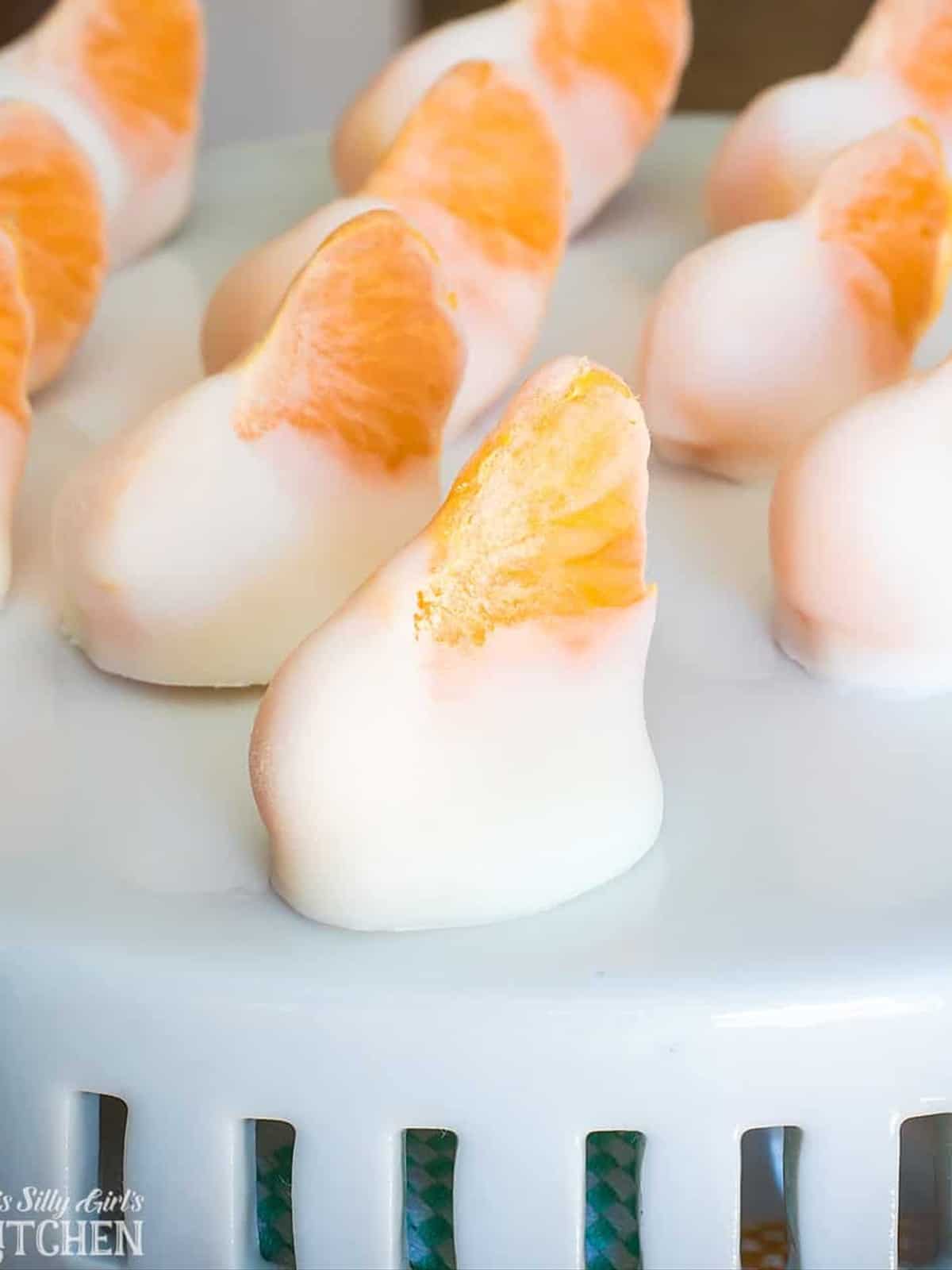 Frozen Yogurt Bites made from clementine segments dipped in vanilla yogurt on a white stand.