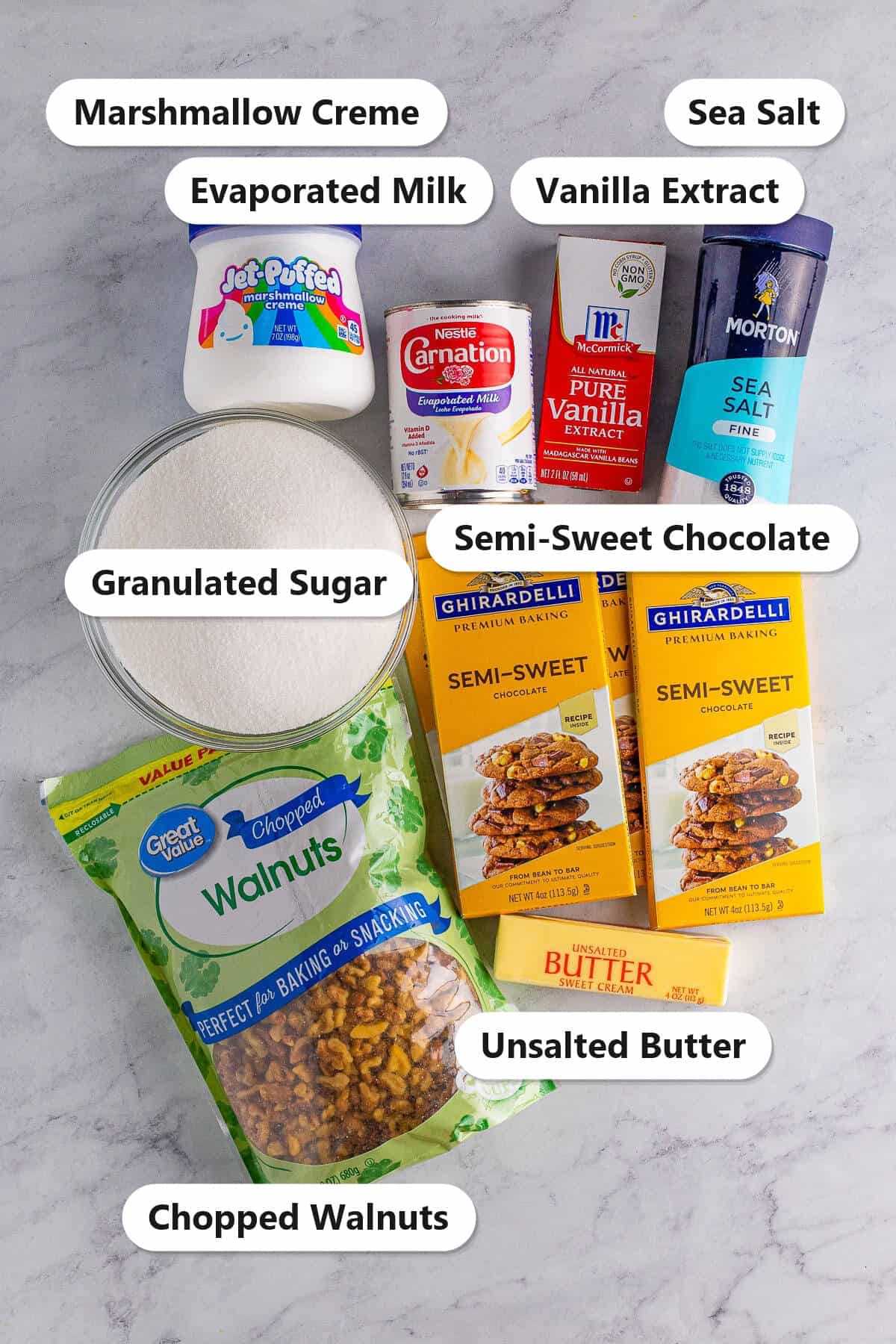 Labeled ingredients for fudge with nuts: semi-sweet chocolate, marshmallow creme, evaporated milk, granulated sugar, butter, vanilla, sea salt, and chopped walnuts.