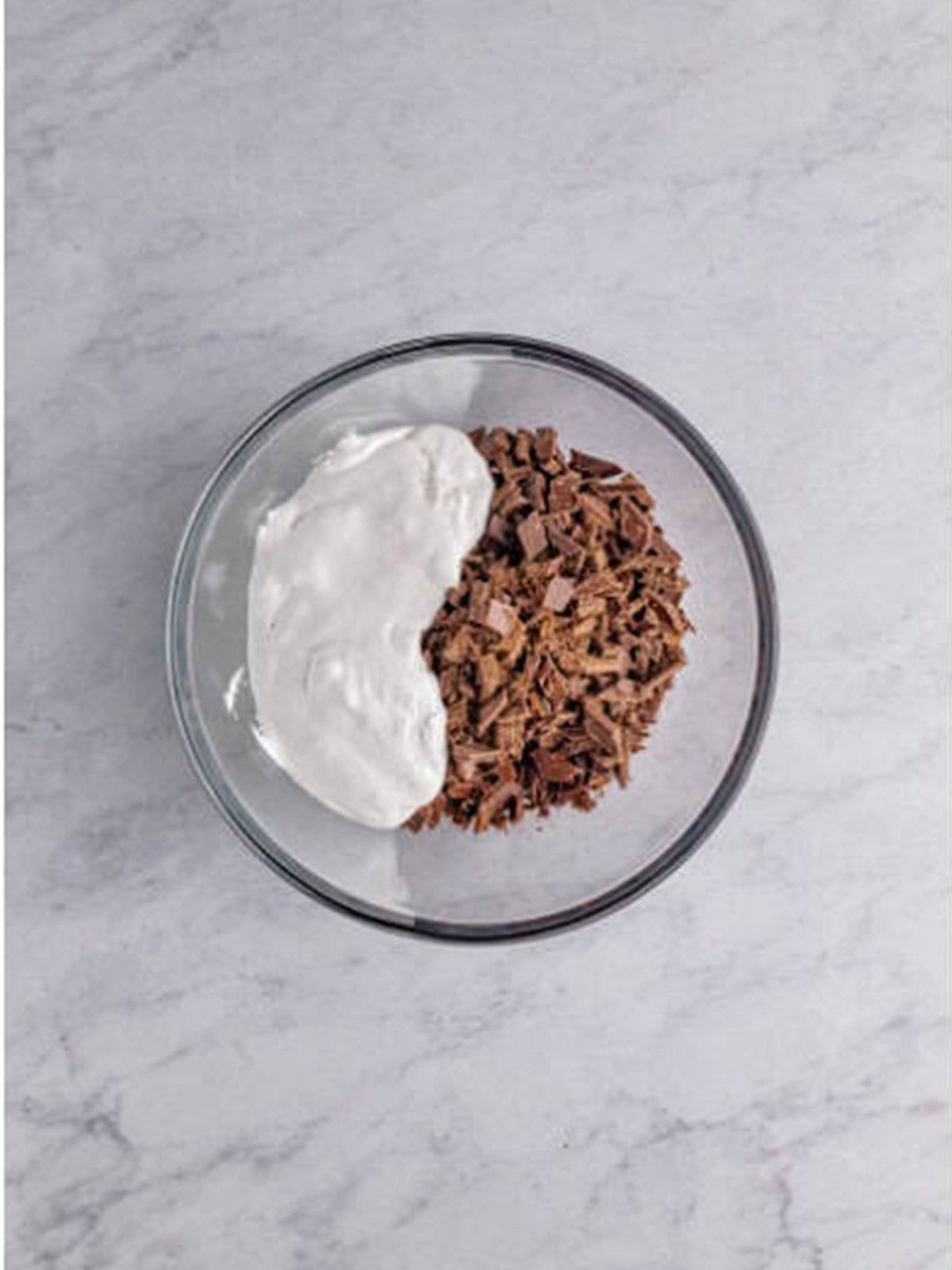 Finely chopped semi-sweet chocolate, marshmallow creme, and vanilla in a large glass bowl for fudge with nuts.