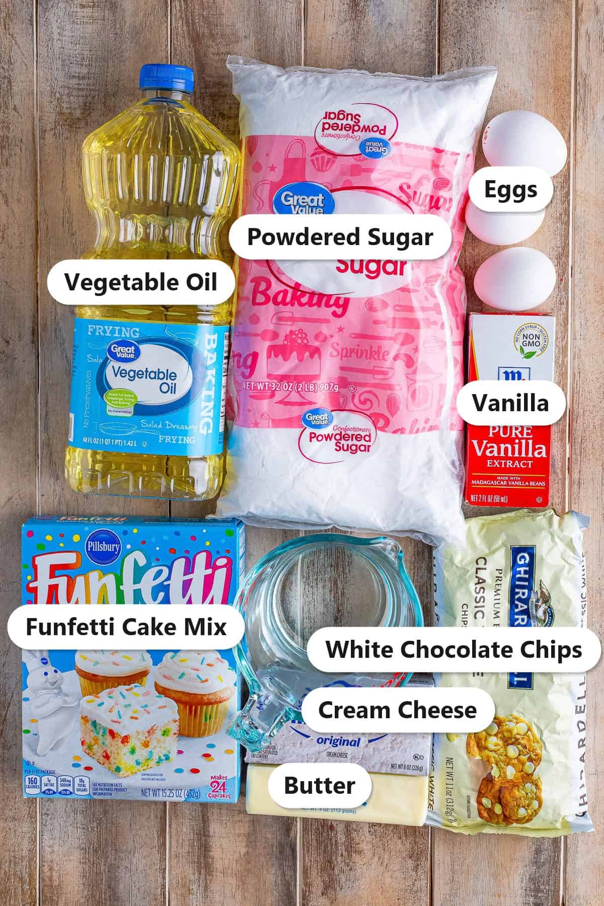 Labeled ingredients to make funfetti earthquake cake including funfetti cake mix, white chocolate chips, cream cheese, butter, powdered sugar, and vanilla.
