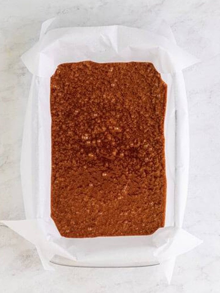 German chocolate brownie batter spread evenly in a parchment lined baking dish.