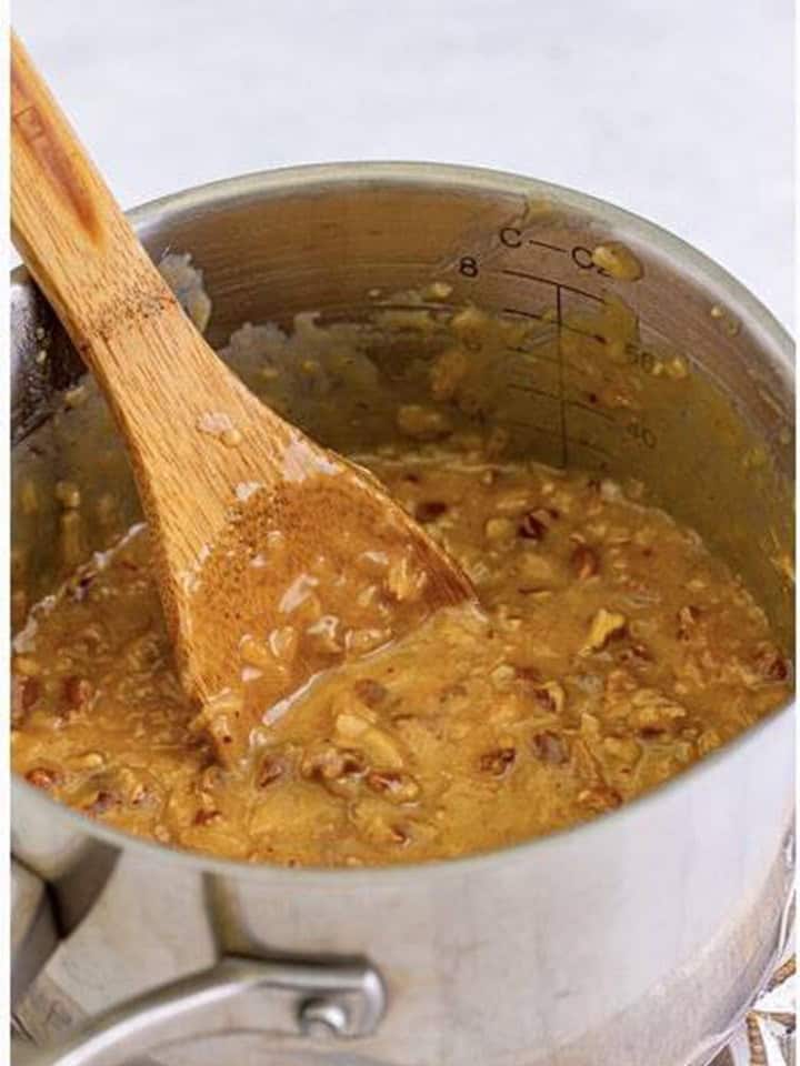Coconut pecan topping simmering in a saucepot with a wooden spoon.