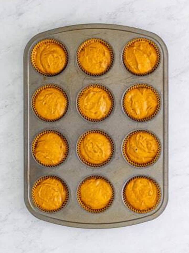 Gingerbread muffin batter divided into a 12 count muffin tin.