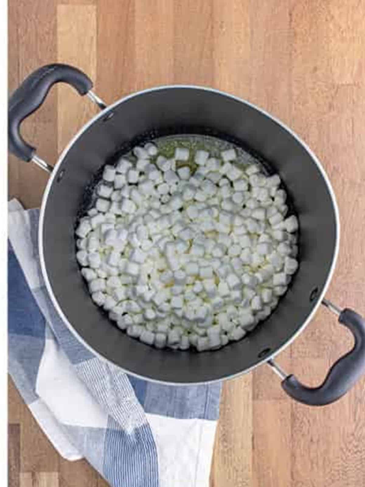 Mini marshmallows added to melted butter in a large pot for golden grahams smores bars.