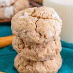 A stack of spiced gooey butter cookies coated in powdered sugar with cinnamon sticks and a glass of milk.
