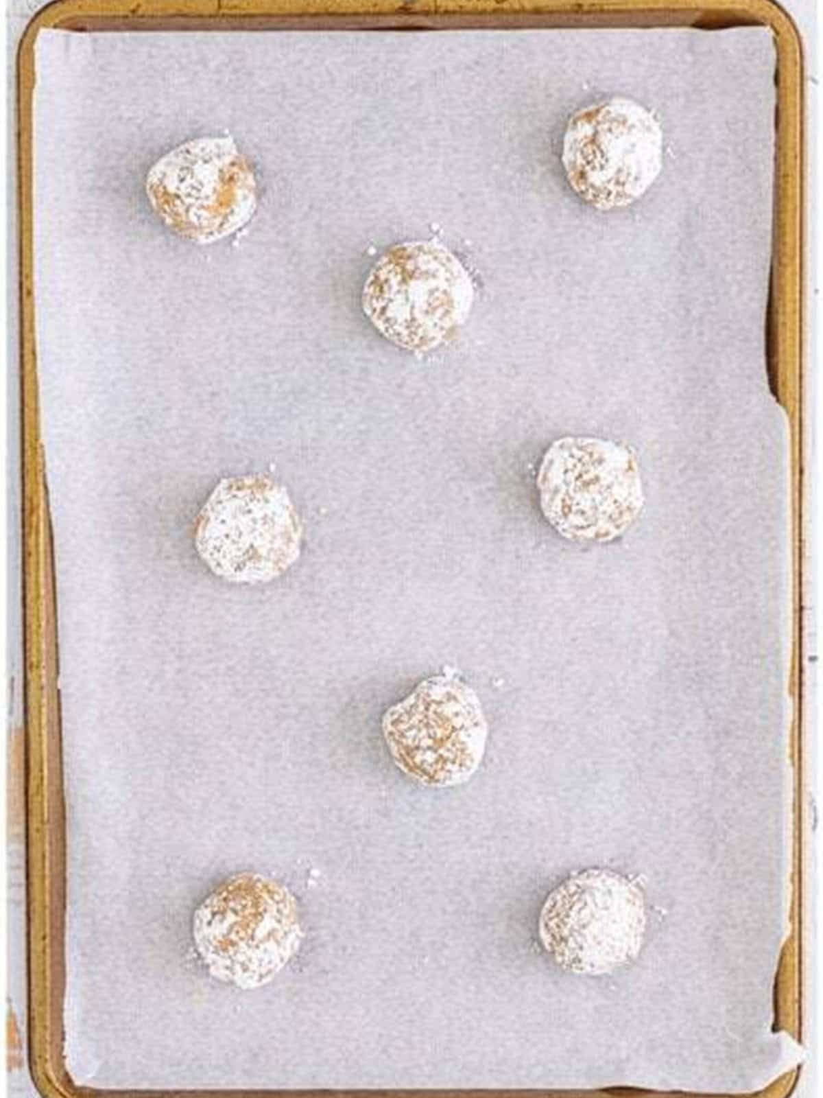 Powdered sugar coated cookie dough balls placed on a parchment lined baking sheet.