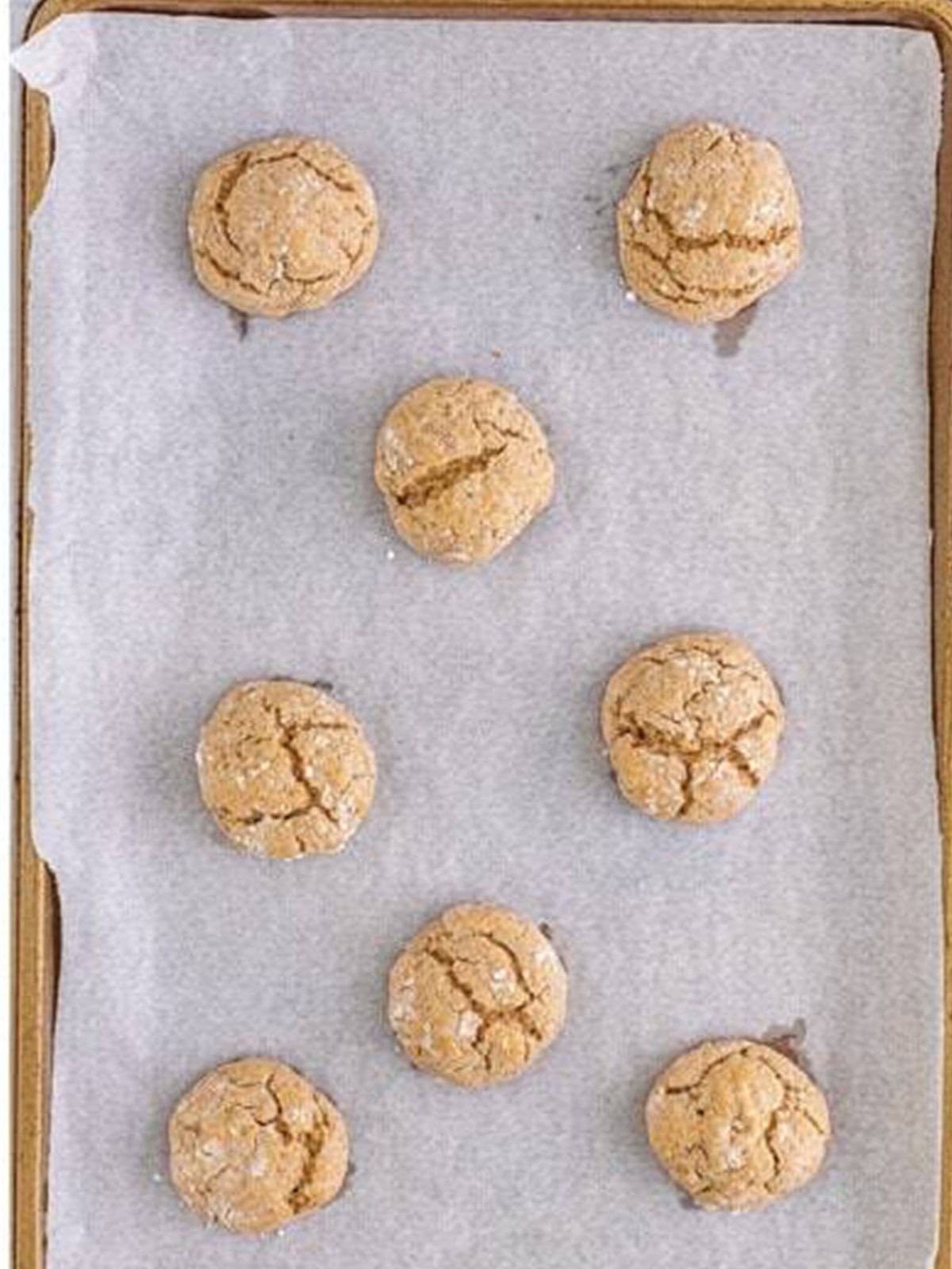 Baked spiced gooey butter cookies with crackled tops on a parchment lined baking sheet.