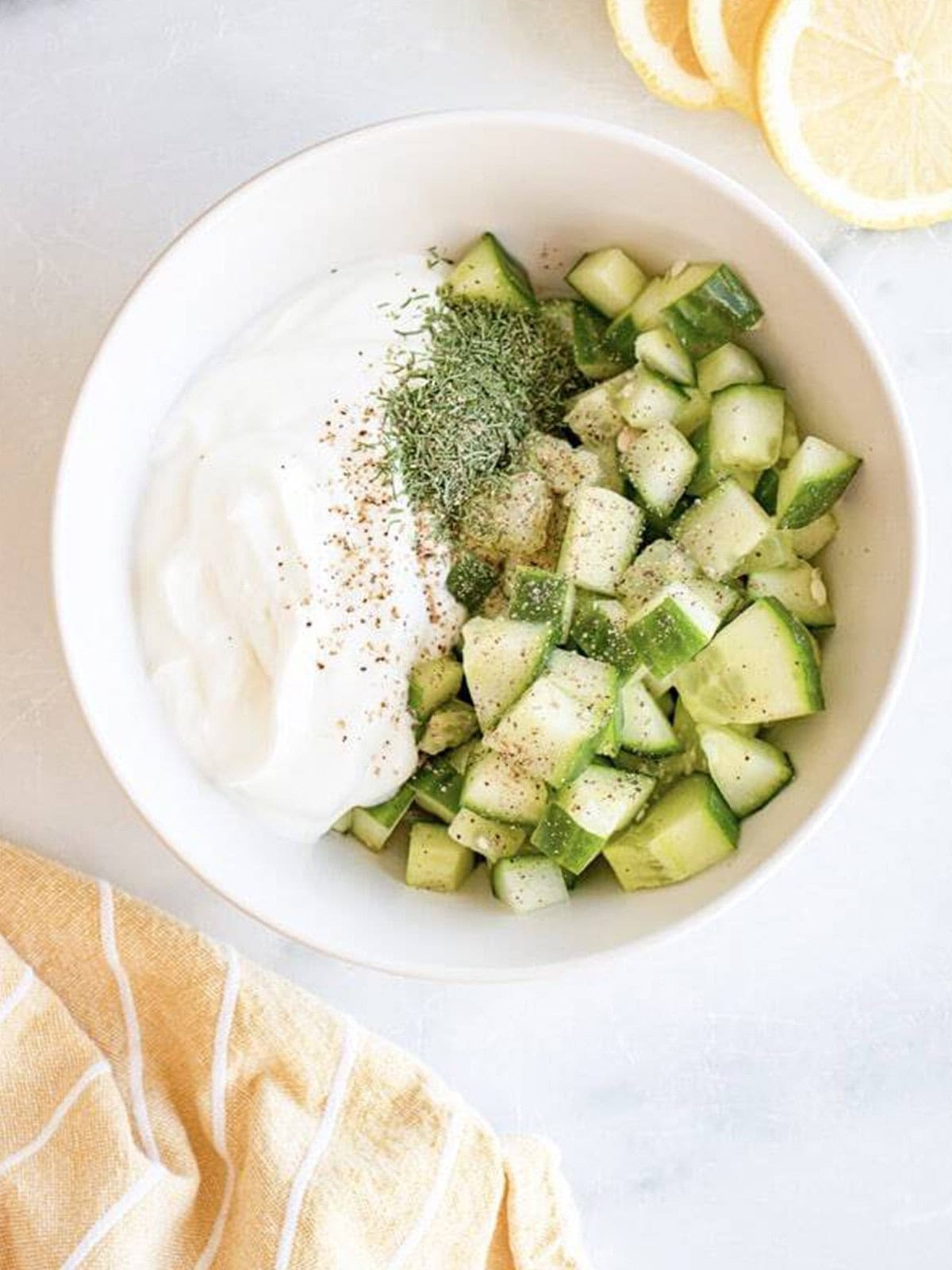 Greek yogurt, diced cucumber, dill, and seasonings in a white bowl for homemade tzatziki sauce.