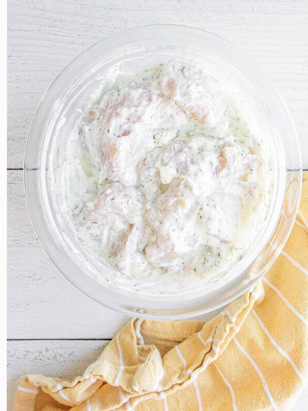 Chicken breast pieces coated in the Greek yogurt marinade in a glass bowl.