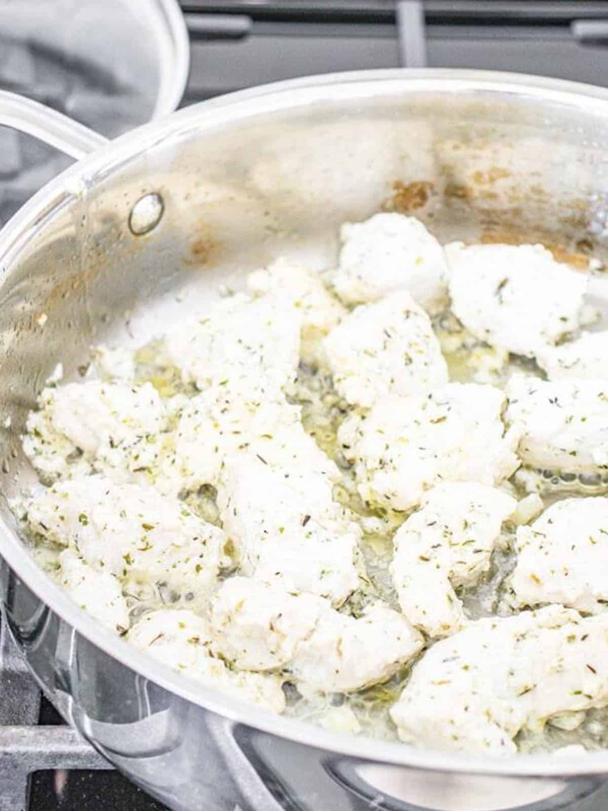 Marinated chicken pieces cooking in a stainless steel skillet on the stove.
