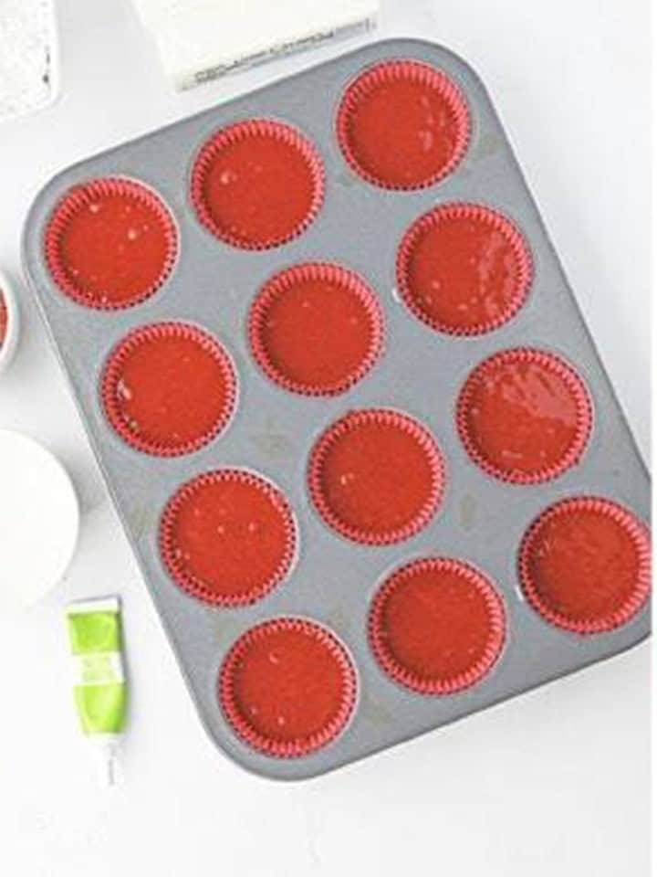Red cupcake liners in a muffin tin filled with red velvet batter.