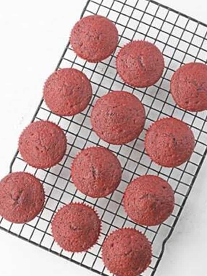 Baked red velvet cupcakes cooling on a wire rack.