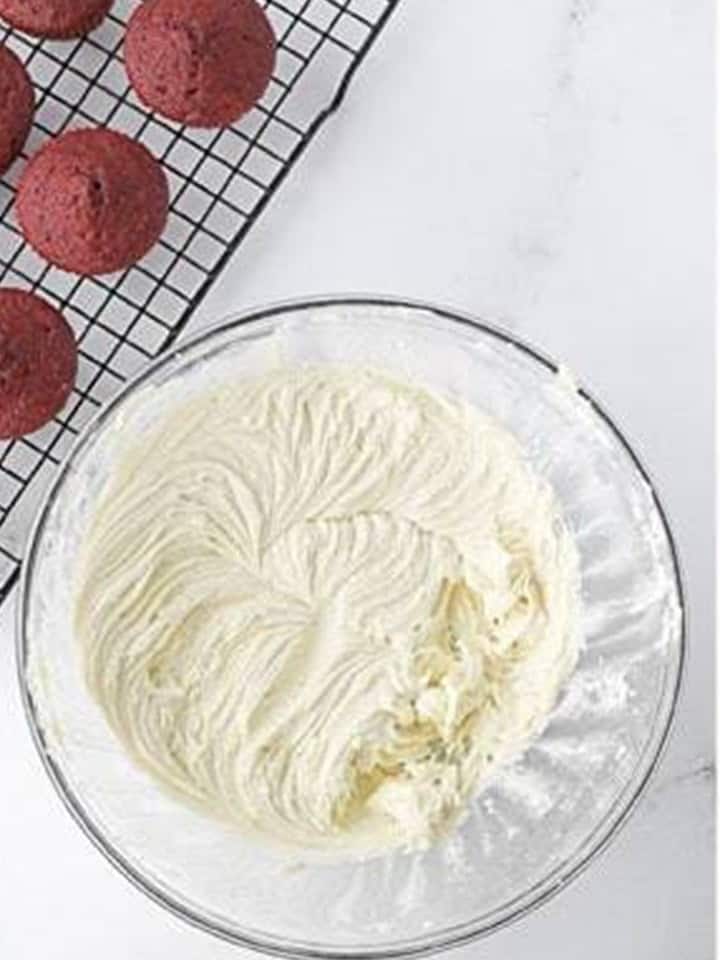 Fluffy white buttercream frosting whipped in a glass bowl.
