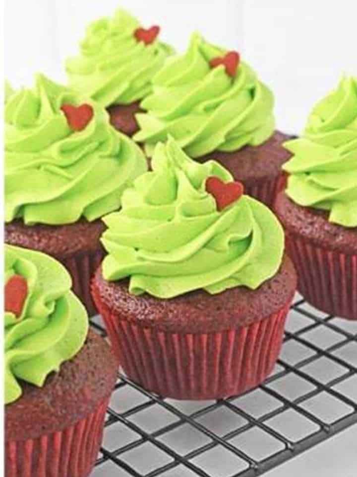 Grinch cupcakes piped with tall green frosting swirls and topped with red heart sprinkles.