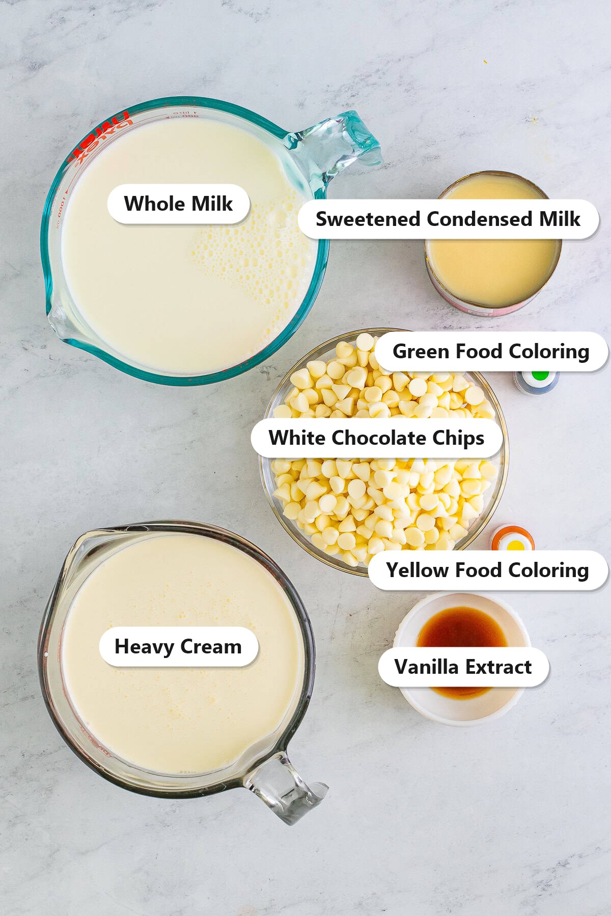 Labeled ingredients for grinch hot cocoa including whole milk, heavy cream, white chocolate chips, sweetened condensed milk, vanilla extract, and green and yellow food coloring.