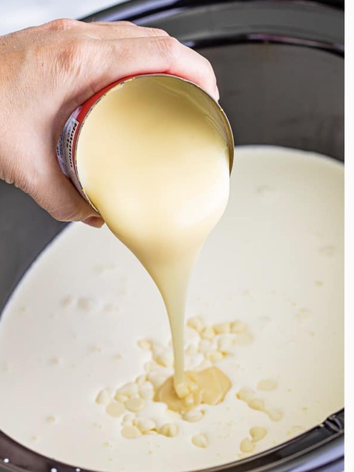 Heavy cream being poured into the slow cooker with the other grinch hot cocoa ingredients.