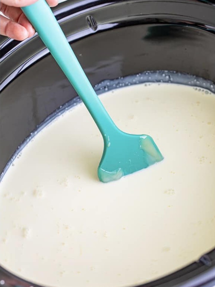 The white hot cocoa base being stirred gently in the slow cooker for grinch hot cocoa.