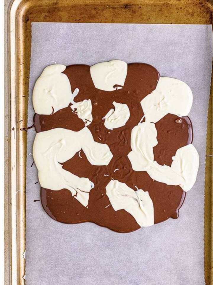Dollops of melted chocolate and white chocolate on a parchment lined sheet tray for halloween bark.
