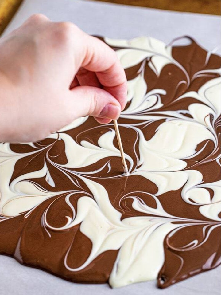 A toothpick swirling the two melted chocolates together into a marble pattern for halloween bark.
