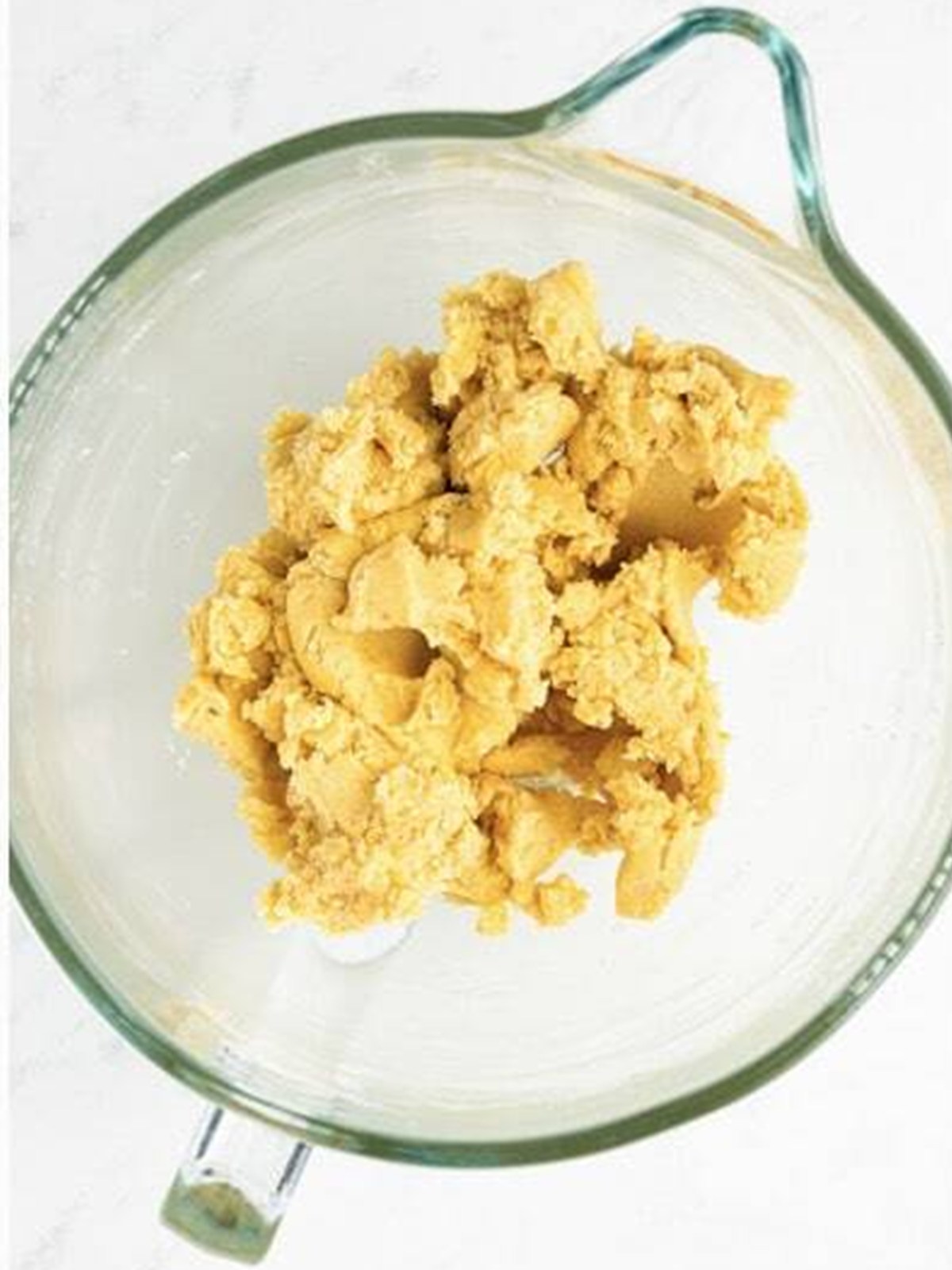 Sugar cookie dough coming together in shaggy clumps in the mixing bowl.
