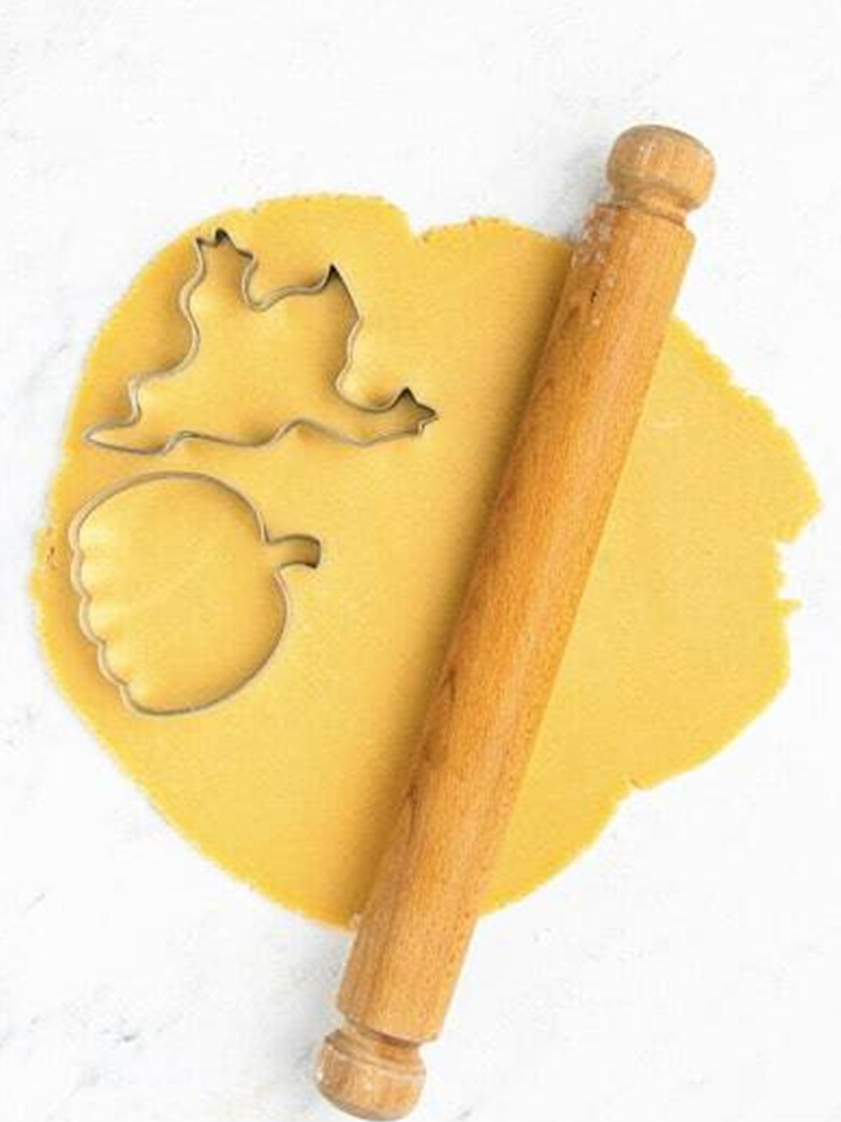 Rolled out sugar cookie dough with ghost and pumpkin cookie cutters and a rolling pin.