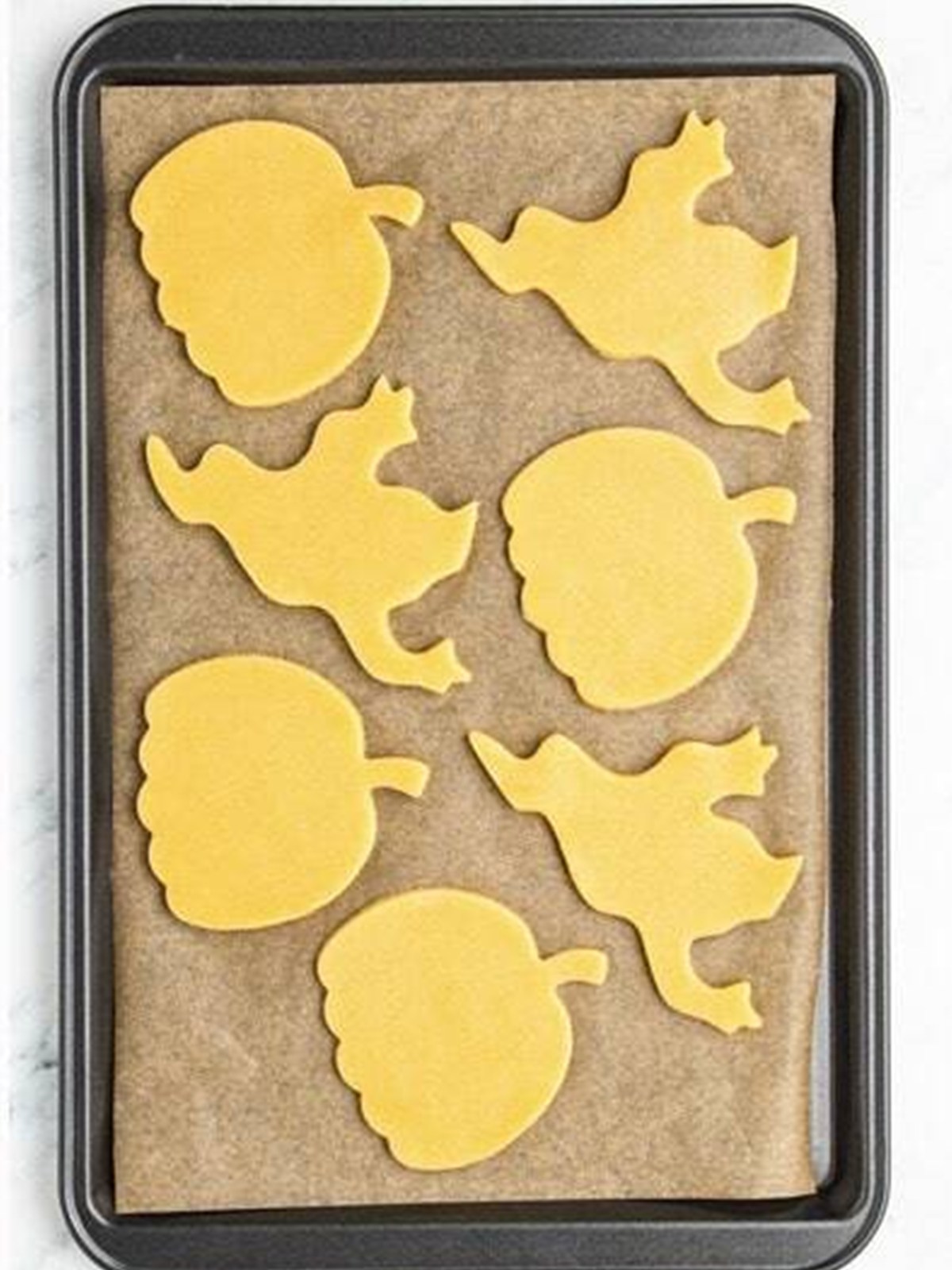 Ghost and pumpkin sugar cookie cutouts arranged on a parchment lined baking sheet.