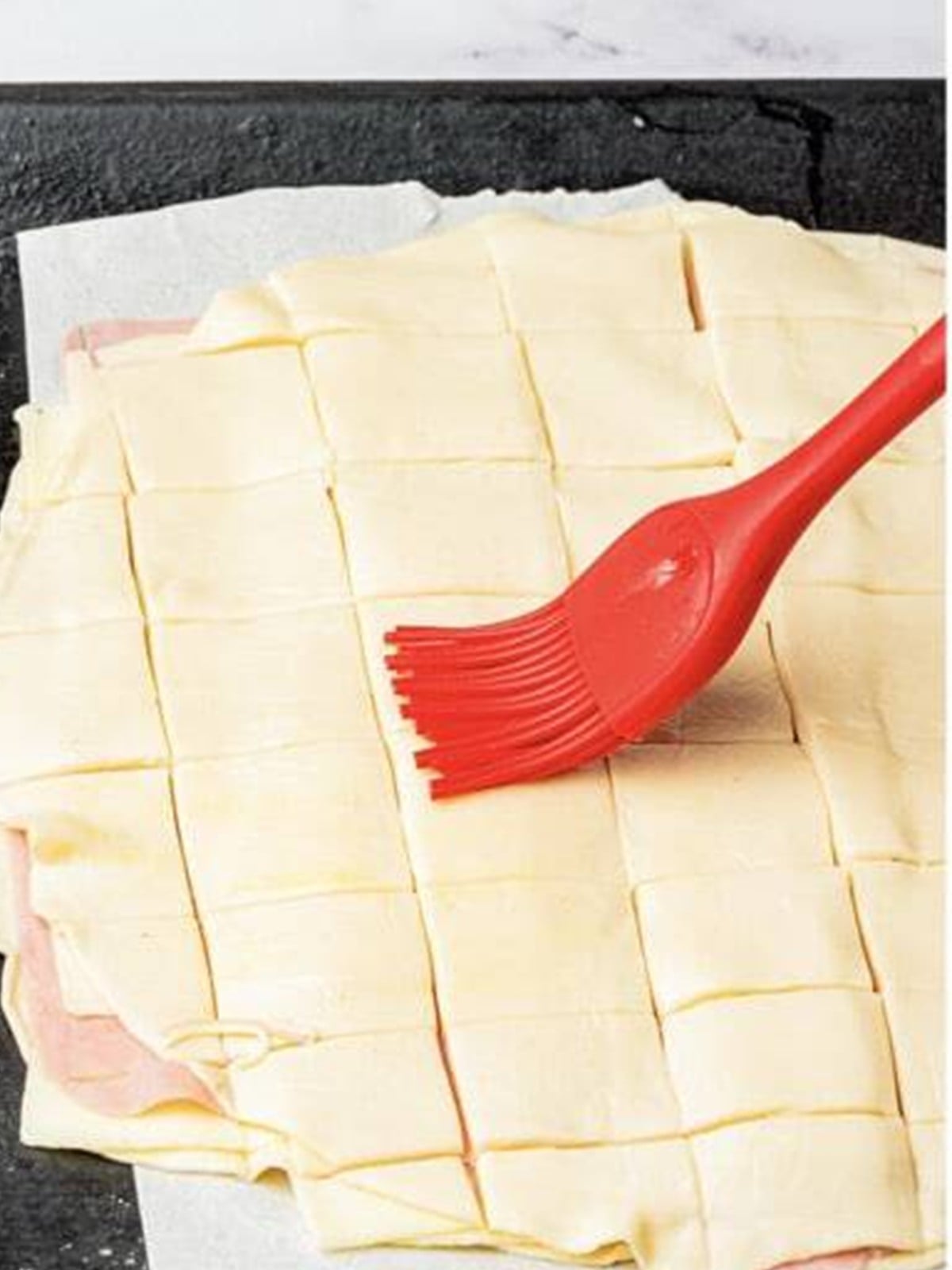 Brushing beaten egg over the scored squares of Ham and Cheese Bars.