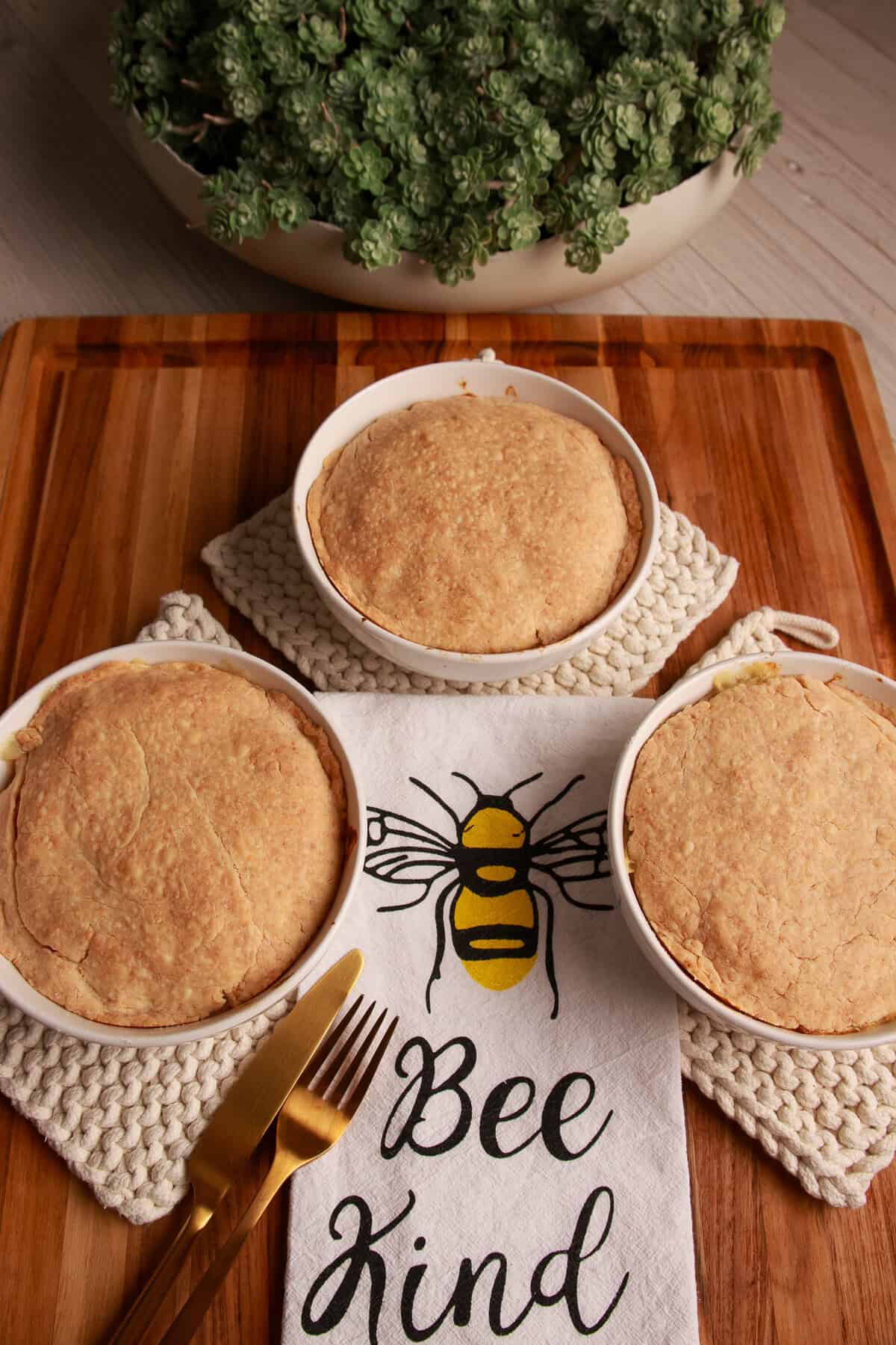 Two Chedz cheesy chicken pot pies with golden cheddar crusts on a Bee Kind kitchen towel.
