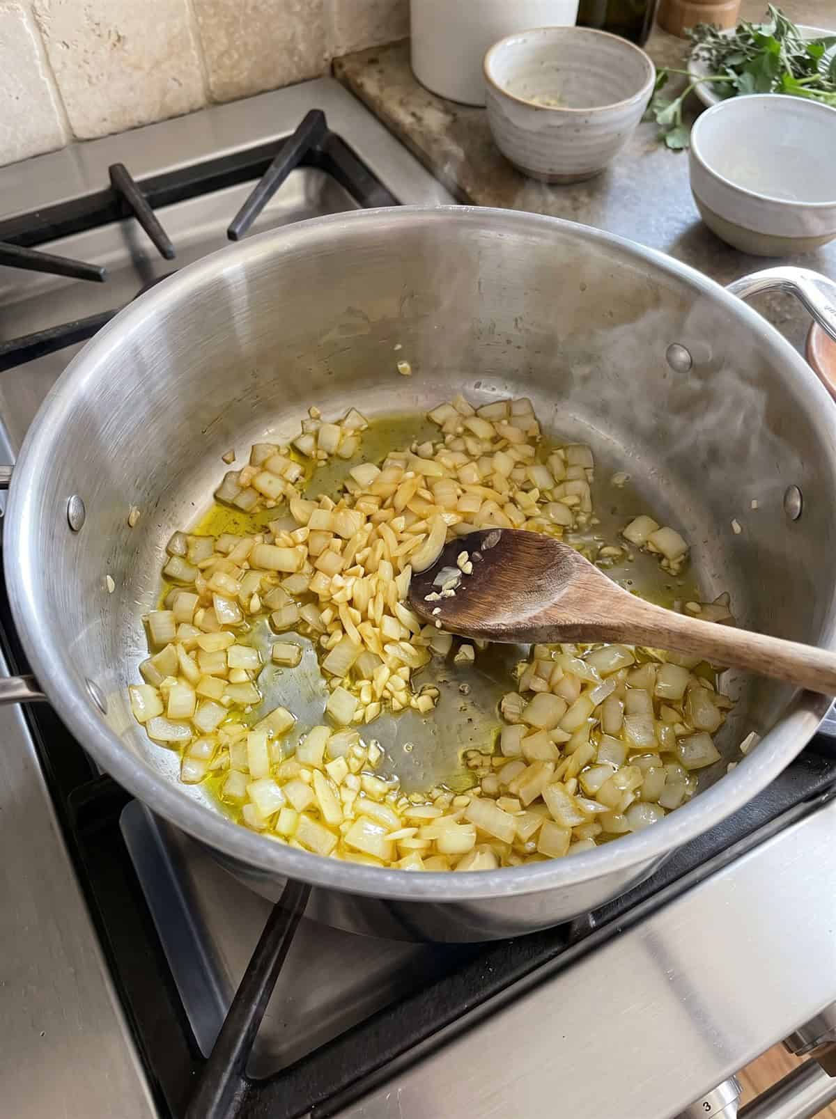 Diced onion and garlic sauteing in olive oil in a large pot for Homemade Pasta Sauce.