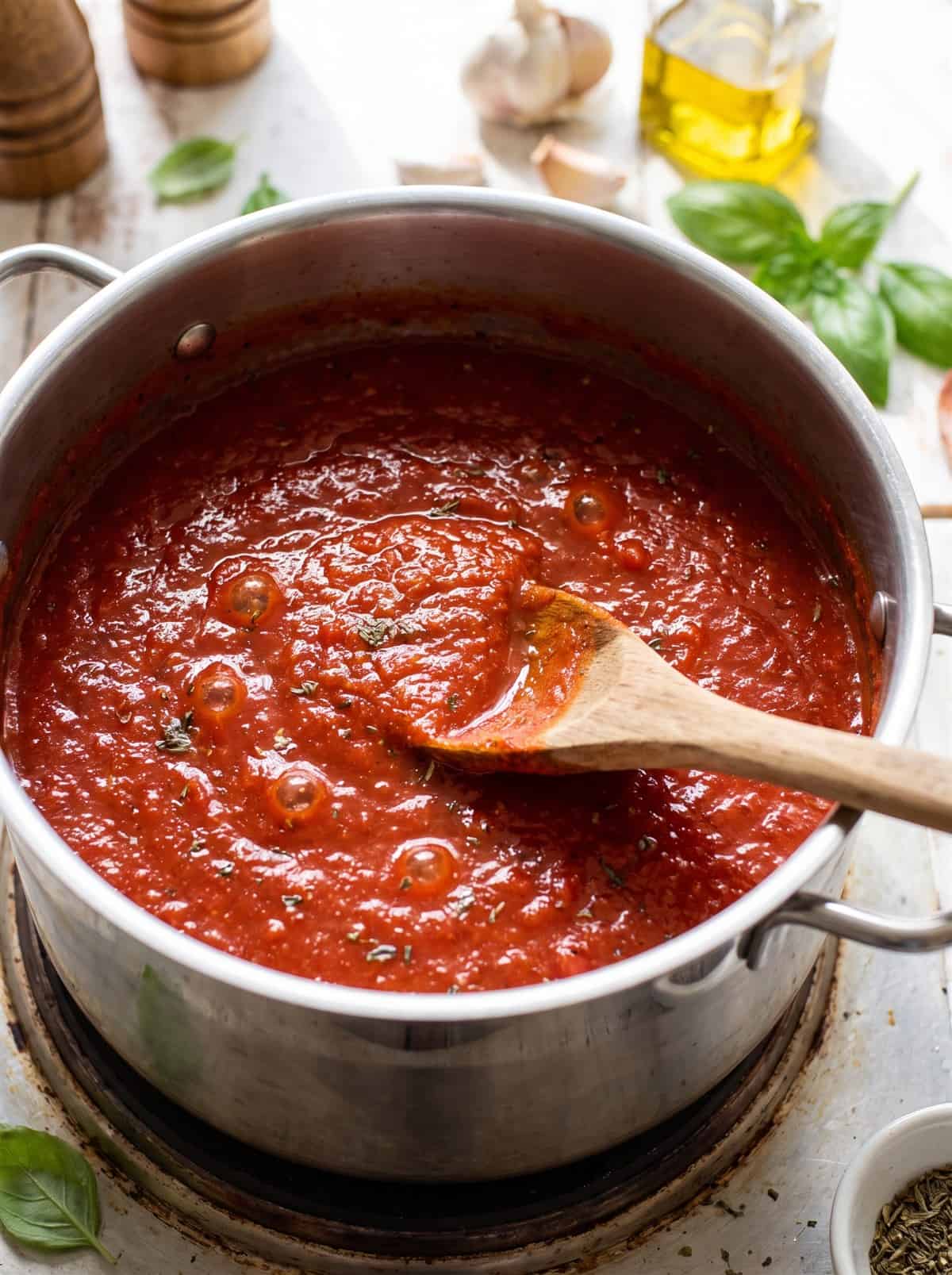 Homemade Pasta Sauce simmering in a pot while being stirred with a wooden spoon.