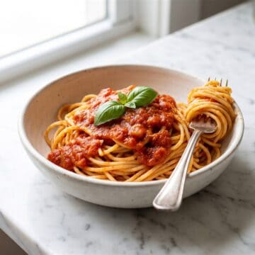 A bowl of spaghetti topped with thick Homemade Pasta Sauce and a fresh basil leaf.