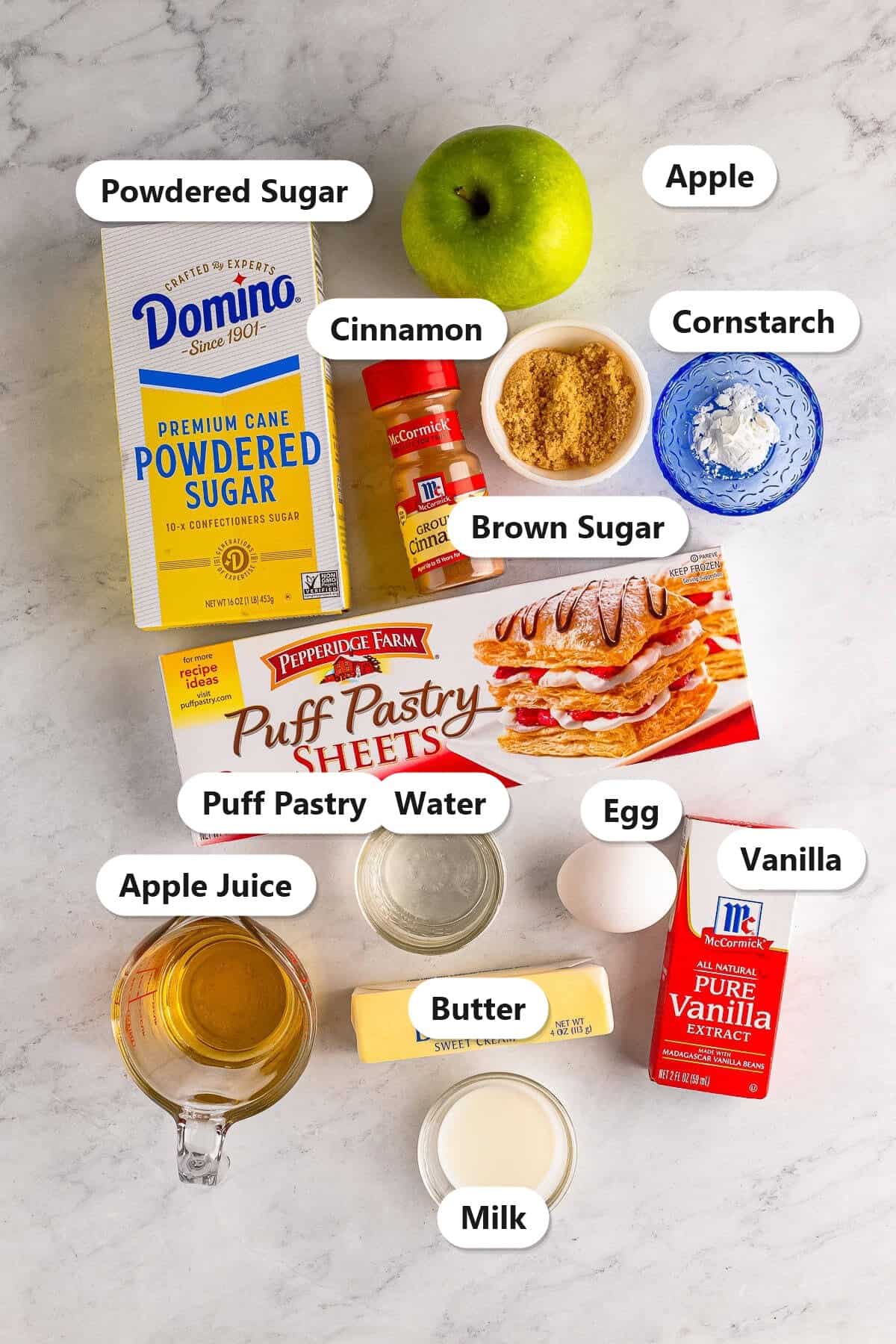 Labeled ingredients for homemade toaster strudel: puff pastry, grated apple, brown sugar, cinnamon, butter, apple juice, cornstarch, egg, powdered sugar, milk, vanilla, and water.